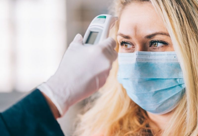 Woman goes through a temperature checks before going to work in the office and wearing medical face mask during COVID-19
